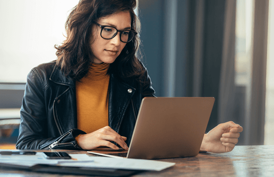 Businesswoman sitting at a table in an office, typing on her laptop with focus.